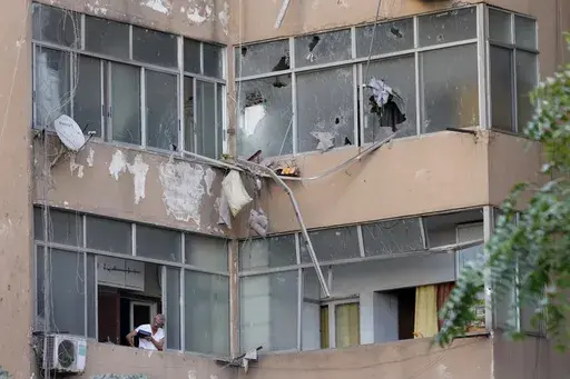 A Lebanese man looks through his apartment window at the scene where an Israeli airstrike hit a building early Monday, Sept. 30, 2024. (AP Photo/Hussein Malla)