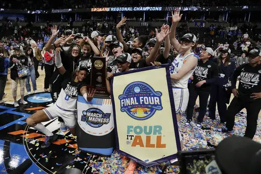 UCLA players and staff surround a trophy and banner for a photograph after their win against LSU in the Elite Eight of the NCAA college basketball tournament, Sunday, March 30, 2025, in Spokane, Wash. (AP Photo/Young Kwak)