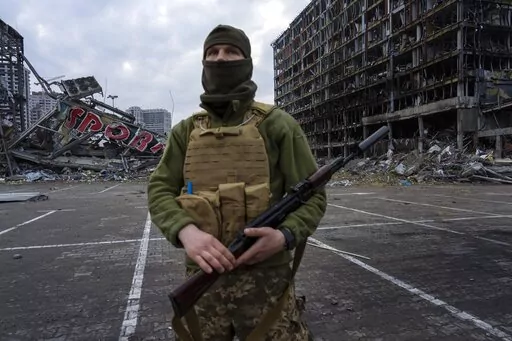 A soldier poses for the picture in Kyiv, Ukraine, Wednesday, March 30, 2022, while standing guard amid the destruction caused after shelling of a shopping center on March 21. (AP Photo/Rodrigo Abd)