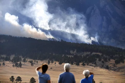 From left, Laura Tyson, Tod Smith and Rebecca Caldwell, residents of Eldorado Springs, watch as the NCAR fire burns in the foothills south of the National Center for Atmospheric Research, Saturday, March 26, 2022, in Boulder, Colo. The NCAR fire prompted evacuations in south Boulder and pre-evacuation warning for Eldorado Springs. According to a study published in Science Advances on Friday, April 1, 2022, a one-two punch of nasty wildfires followed by heavy downpours, triggering flooding and mu