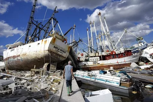Bruce Hickey, 70, walks along the waterfront, now littered with debris including shrimp boats, in the mobile home park where he and his wife, Kathy, have a winter home on San Carlos Island, Fort Myers Beach, Fla., on Oct. 5, 2022, one week after the passage of Hurricane Ian. (AP Photo/Rebecca Blackwell)