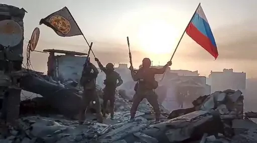 In this image taken from video and released on Saturday, May 20, 2023, by the press service of Yevgeny Prigozhin, head of the Wagner private military contractor, his forces wave Russian and Wagner flags atop a damaged building in Bakhmut, Ukraine. Some convicts recruited by Wagner to fight in in Ukraine are coming home to Russia and committing new crimes. That has raised fears in communities where the now-freed convicts are returning, and reports of killings, robberies and sexual assaults by som