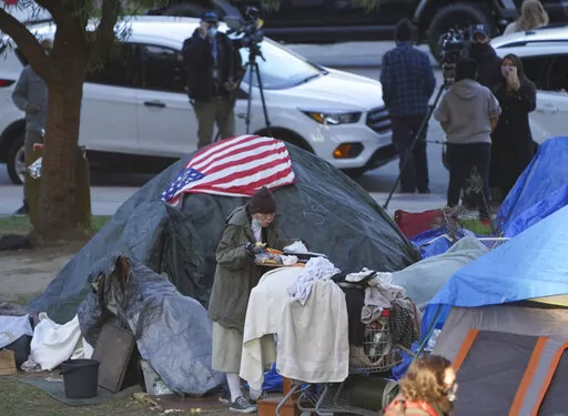 A woman eats at her tent at the Echo Park homeless encampment at Echo Park Lake in Los Angeles, on March 24, 2021. From homelessness to rising crime, Los Angeles residents are unhappy and frustrated. The campaign for the city's next mayor will test if voters in the liberal-minded city could embrace a new mayor with a tough approach to crime and sprawling homeless encampments that have spread into virtually every neighborhood.  (AP Photo/Damian Dovarganes, File)
