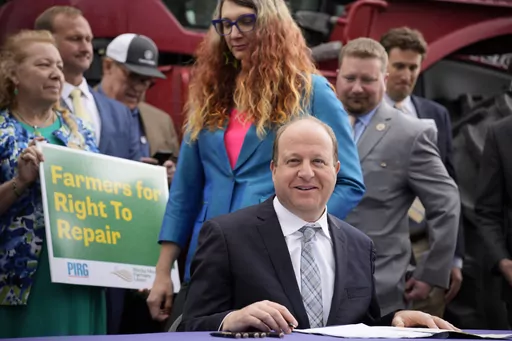 Colorado Gov. Jared Polis, front, waits to sign legislation that forces manufacturers to provide the necessary manuals, tools, parts and even software to farmers so they can fix their own machines, Tuesday, April 25, 2023, during a ceremony outside the State Capitol in Denver. Colorado is the first state to put the right-to-repair law into effect while at least 10 other states are considering similar measures. Colorado State Rep. Brianne Titone, center, and Rep. Ron Weinberg, back, head in to wi