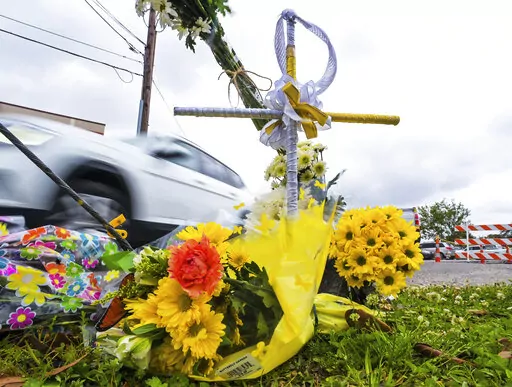 A collection of flowers and a cross with a halo are seen at the location where the body of Linda Frickey was recovered after she was carjacked and dragged to her death a day earlier on N. Pierce Street in New Orleans, Tuesday, March 22, 2022. New Orleans Police Department Superintendent Shaun Ferguson announced that four teenagers allegedly involved in the death of Frickey, 73, have been arrested. (Max Becherer/The Times-Picayune/The New Orleans Advocate via AP)