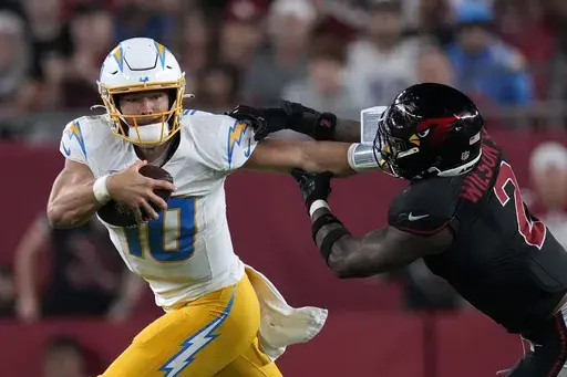 Los Angeles Chargers quarterback Justin Herbert (10) runs from Arizona Cardinals linebacker Mack Wilson Sr. (2) during the second half of an NFL football game, Monday, Oct. 21, 2024, in Glendale Ariz. (AP Photo/Matt York)
