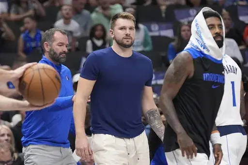 An injured Dallas Mavericks guard Luka Doncic, center, looks on from the sidelines as teammate Kyrie Irving, right, walks off during the first half of a preseason NBA basketball game against the Utah Jazz Thursday, Oct. 10, 2024, in Dallas. (AP Photo/LM Otero)