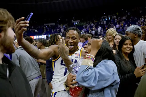 LSU guard Trae Hannibal takes a photo with one of fans who rushed the court after LSU's victory over Kentucky in an NCAA college basketball game in Baton Rouge, La., Wednesday, Feb. 21, 2024. (AP Photo/Matthew Hinton)