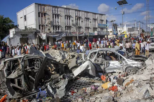People walk amidst destruction at the scene, a day after a double car bomb attack at a busy junction in Mogadishu, Somalia Sunday, Oct. 30, 2022. Somalia's president says multiple people were killed in Saturday's attacks and the toll could rise in the country's deadliest attack since a truck bombing at the same spot five years ago killed more than 500. (AP Photo/Farah Abdi Warsameh)