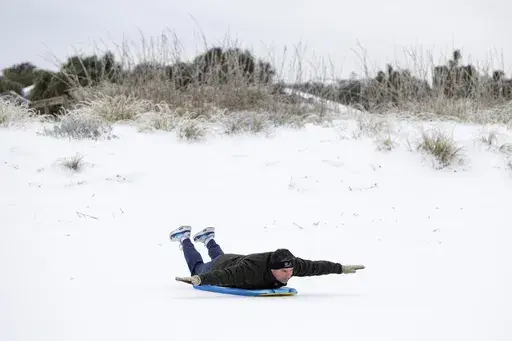 Alex Spiotta, from the Isle of Palms, S.C., uses a boogie board to sled across the beach after a winter storm dropped ice and snow Wednesday, Jan. 22, 2025, on the Isle of Palms, S.C. (AP Photo/Mic Smith)