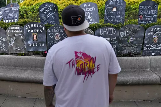 A man looks at cardboard gravestones with the names of victims of opioid abuse outside the courthouse where the Purdue Pharma bankruptcy is taking place in White Plains, N.Y., Monday, Aug. 9, 2021.  A federal appeals panel is scheduled to hear arguments on whether members of the Sackler family can be granted protection from lawsuits as part of a bankruptcy settlement for the company they own, OxyContin maker Purdue Pharma. If the company doesn’t get what it wants, it could have to fight off th