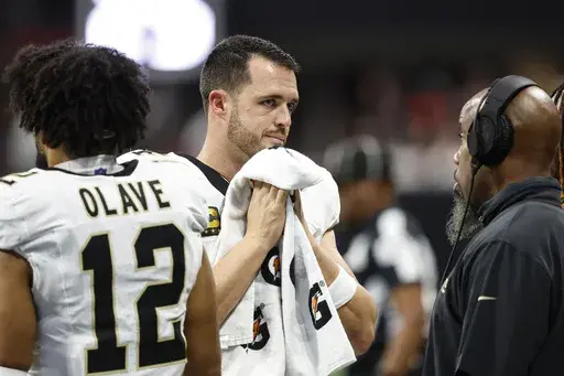 New Orleans Saints quarterback Derek Carr, center, speaks on the sidelines during the second half of an NFL football game against the Atlanta Falcons, Sunday, Sept. 29, 2024, in Atlanta. (AP Photo/Butch Dill)