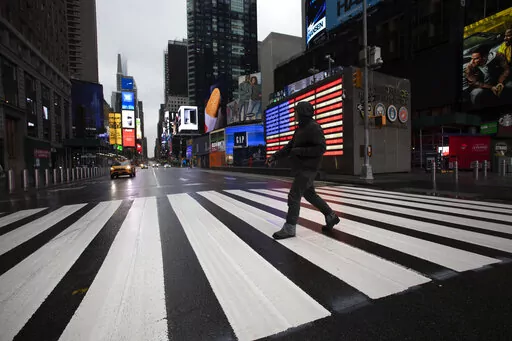 A man crosses the street in a nearly empty Times Square, which is usually very crowded on a weekday morning in New York on March 23, 2020. (AP Photo/Mark Lennihan, File)