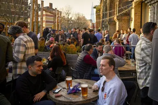 People sit in the sun outside a bar on the Bermondsey Beer Mile in south London, Saturday March 8, 2025. (AP Photo/Tony Hicks)