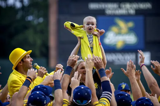 Molly Knutson holds her baby James Knutson high above the players as the Savannah Bananas present the Banana Baby to the crowd while playing the theme song from the movie "Lion King" over the public address system, Saturday, June 11, 2022, in Savannah, Ga. (AP Photo/Stephen B. Morton)