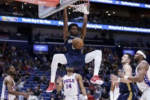New Orleans Pelicans forward Keion Brooks Jr., top, hangs from the rim after dunking against Philadelphia 76ers guard Ricky Council IV (14) during the first half of an NBA basketball game in New Orleans, Monday, March 24, 2025. (AP Photo/Matthew Hinton)
