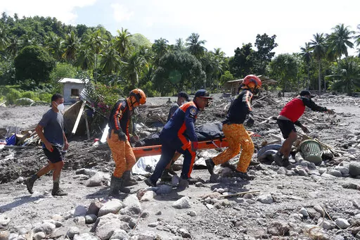 Rescuers carry a body at Maguindanao's Datu Odin Sinsuat town, southern Philippines on Sunday Oct. 30, 2022. Victims of a huge mudslide set off by Tropical Storm Nalgae in a coastal Philippine village that had once been devastated by a killer tsunami mistakenly thought a tidal wave was coming and ran to higher ground toward a mountain and were buried alive, an official said Sunday. (AP Photo)