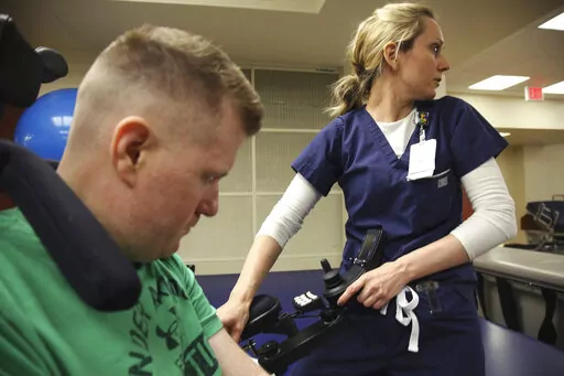 In this July 6, 2017 photo, occupational therapist Ashley Broadwater, waits for help to sit Cpl. Nick Tullier on a bed so he can begin his physical rehabilitation at TIRR Memorial Hermann Hospital in Houston.   Tullier, a Baton Rouge sheriff’s deputy who was shot in the head and stomach during a July 2016 ambush that killed three other law enforcement officers during a summer of protests over the police killing of a Black man, died Thursday, May 5, 2022, at age 47. Tullier's death was announce