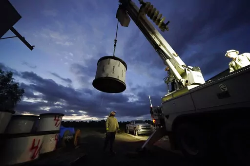 FILE- A worker stands by to guide a spool of electrical wire being loaded onto his truck before heading out at dawn, inside a tent city for electrical workers in Amelia, La., on Sept. 17, 2021. Louisiana’s largest power company is asking the Federal Emergency Management Agency for $450 million to make its electric grid more resilient, under a program to help communities prepare for hurricanes and other extreme weather. Entergy Corp.’s eight grant applications include three of the four projec