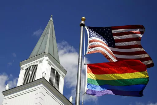 A gay pride rainbow flag flies along with the U.S. flag in front of the Asbury United Methodist Church in Prairie Village, Kan, on April 19, 2019.  A group of theologically conservative United Methodists plans to launch a new worldwide denomination on May 1, 2022.  This will begin the breakup of the third-largest religious body in the U.S.  (AP Photo/Charlie Riedel, File)