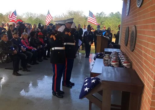 Marine honor guard members salute urns containing the ashes of veterans awaiting entombment at the Northwest Louisiana Veterans Cemetery Thursday, Feb. 17, 2022. Thirteen veterans who died in recent years but whose remains were never claimed have been honored in a funeral service in northern Louisiana, as a crowd of people who didn't know them but who wanted to pay their respects looked on. (John Prime via AP)