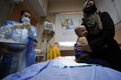 A woman holds her crying child at the cancer ward of the Children's Hospital in Damascus, Syria, Monday, March. 7, 2022. More than a decade of war has brought the Syrian health sector close to collapse, and an economic crisis has meant that cancer treatment is either unaffordable or in short supply. A private charity, Basma, offers cancer treatment without charge to impoverished Syrian children. (AP Photo/Omar Sanadiki)