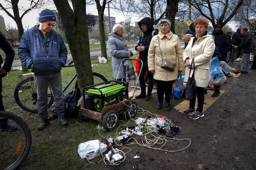 Local residents gather near a generator to charge their mobile devices in an area controlled by Russian-backed separatist forces in Mariupol, Ukraine, Friday, April 22, 2022. When Russian forces two months ago launched a military campaign against infrastructure in Ukraine, it opened an urgent second front far from the contact line: Along power lines, water mains, and heating systems, and in places like homes, schools, offices and churches. (AP Photo/Alexei Alexandrov, File)