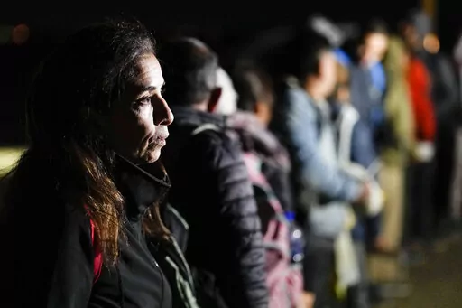 A woman from Cuba waits with other migrants to be processed to seek asylum after crossing the border into the United States, Friday, Jan. 6, 2023, near Yuma, Ariz. An underground market has emerged for migrants seeking U.S. sponsors since the Biden administration announced last month that it would accept a limited number of people from Venezuela, Cuba, Nicaragua and Haiti. Applicants for the humanitarian parole program need someone in the U.S. to promise to provide financial support for at least
