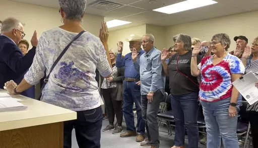 In this image from video, Nye County Clerk Mark Kampf, far left, in suit, swears in a group of residents who will hand count early ballots cast in the rural county about halfway between Las Vegas and Reno, on Wednesday, Oct. 26, 2022, in Pahrump, Nev. Nye is the largest county in the U.S. to attempt a hand count of all its ballots in the midterm elections, a change fueled by conspiracy theories about voting machines. (AP Photo/Gabe Stern