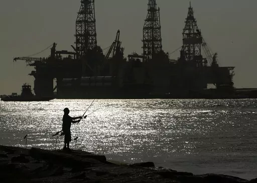 A man wears a face mark as he fishes near docked oil drilling platforms, on May 8, 2020, in Port Aransas, Texas. A federal court has rejected a proposed lease auction for offshore oil drilling in the Gulf of Mexico, saying the Biden administration failed to conduct a proper environmental review. The decision on Jan. 27, 2022, by U.S. District Judge Rudolph Contreras sends the proposed lease sale back to the Interior Department to decide next steps. (AP Photo/Eric Gay, File)
