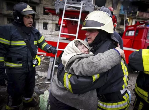In this photo released by Ukrainian State Emergency Service, a firefighter hugs an elderly woman after evacuation from an apartment building hit by shelling in Kyiv, Ukraine, Monday, March 14, 2022. (Ukrainian State Emergency Service via AP)