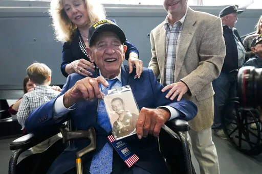 World War II veteran Joseph Eskenazi, who at 104 years and 11 months old is the oldest living veteran to survive the attack on Pearl Harbor, holds a photo of his younger self, at an event celebrating his upcoming 105th birthday at the National World War II Museum in New Orleans, Wednesday, Jan. 11, 2023. (AP Photo/Gerald Herbert)