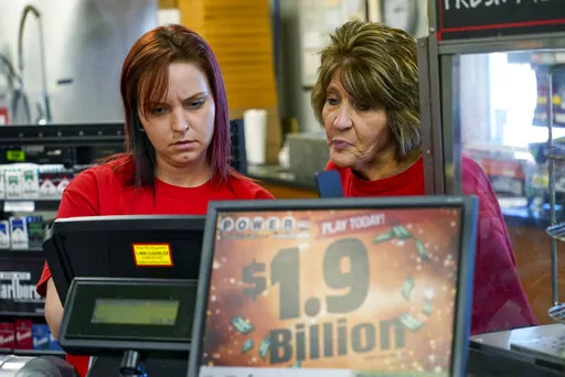 Della Reminar, right, and Crystal Baptiste try to get the ticket machine to scan a card for personal selection numbers for a ticket for the Monday Powerball drawing with an annuity value of at least $1.9 billion, Monday, Nov. 7, 2022, at a convenience store in Renfrew, Pa. (AP Photo/Keith Srakocic)
