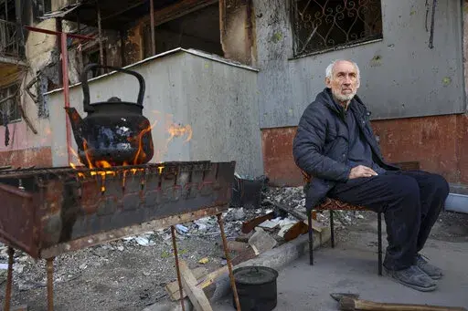 A local man sits in front of an apartment building damaged from heavy fighting as he waits for the kettle to boil in an area controlled by Russian-backed separatist forces in Mariupol, Ukraine, Tuesday, April 26, 2022. (AP Photo/Alexei Alexandrov)