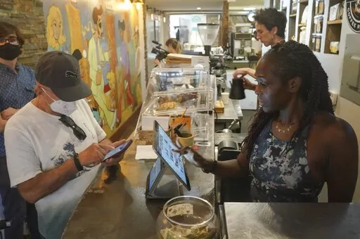 Kymme Williams-Davis, right, takes orders at the Bushwick Grind Café she owns, Thursday Sept. 8, 2022, in New York. Williams-Davis has noticed a definite shift in customer demand since she's had to raise prices and switch to different types of goods to keep up with inflation. (AP Photo/Bebeto Matthews)