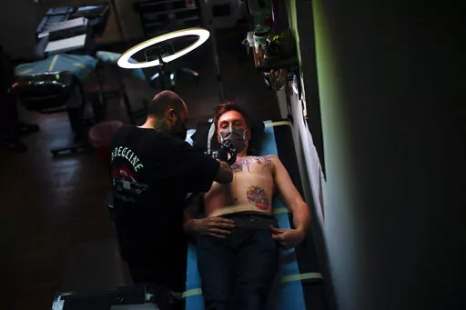 A man, wearing a protective face mask to prevent the spread of coronavirus, is tattooed at Paul and Friends tattoo parlour in downtown Brussels, March 26, 2021. The European Union is imposing restrictions on the inks that tattoo artists can use as of Wednesday, Jan. 5, 2022. The EU says it is a necessary move to protect the health of consumers because thousands of chemical elements now in use can cause anything from allergic reactions to cancer. The tattoo industry complains it is unfairly targe