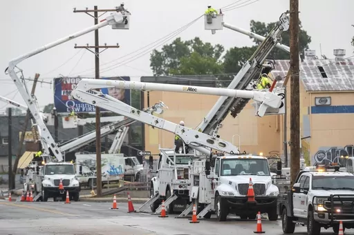 Line workers in boom trucks and on the street work to replace broken utility poles and lines as rain moves in on Peoria Avenue over the Broken Arrow Expressway, Wednesday, June 21, 2023, in Tulsa, Okla. (Daniel Shular/Tulsa World via AP)