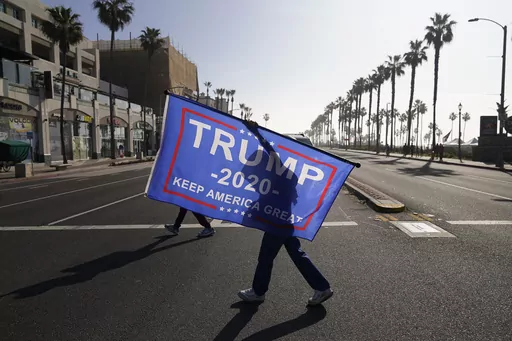 A woman walks across the street with a flag supporting President Donald Trump during a rally Jan. 6, 2021, in Huntington Beach, Calif. A state GOP rule change has opened the possibility that former President Donald Trump could sweep California’s entire trove of delegates in the March 5 primary, the plumpest prize in the party’s nominating contest. The election falls on Super Tuesday, when California is among more than a dozen states holding primaries and the largest number of delegates are u