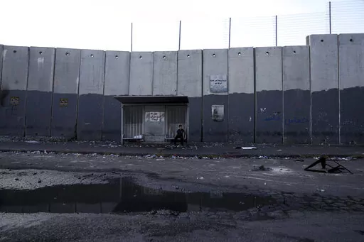 A child sits at a bus stop in the besieged Shuafat refugee camp in east Jerusalem, Thursday, Oct. 13, 2022.It was the site of fierce clashes after Israeli security forces set up checkpoints that choked off the only exit and entry points of the camp during a manhunt following the death of a soldier, bringing life to a standstill for its estimated 60,000 residents. (AP Photo/Mahmoud Illean)