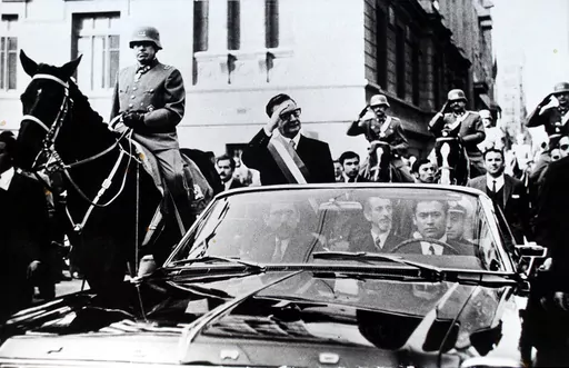 Chilean President Salvador Allende salutes from an open vehicle as General Augusto Pinochet rides on horseback at left in Santiago, Chile, May 21, 1972. (AP Photo/File)