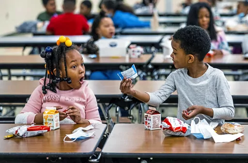 First graders, from left, Kendal Kates and Ryan Kenney are excited about the contents of their boxed lunches at Langley K-8 School, Dec. 23, 2021, in the Sheraden neighborhood in Pittsburgh. The Biden administration has issued transitional standards for school lunches that are meant to get cafeterias back on a healthier course as they recover from pandemic and supply chain disruptions.  The “bridge” rule announced by the U.S. Agriculture Department on Friday extends emergency flexibilities f
