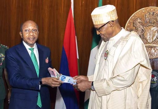 In this photo released by the Nigeria State House, Nigeria's central bank governor, Godwin Emefile, left, presents the newly designed currency notes to Nigeria's President Muhammadu Buhari, right, during a launch in Abuja, Nigeria, Tuesday, Nov. 22, 2022. Nigeria has unveiled newly designed currency notes that the West African nation’s central bank says will help curb inflation and money laundering. (Sunday Aghaeze/Nigeria State House via AP)