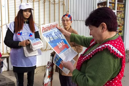 A volunteer of Luhansk regional election commission distributes newspapers to local citizens prior to a referendum in Luhansk, Luhansk People's Republic controlled by Russia-backed separatists, eastern Ukraine, Thursday, Sept. 22, 2022. Authorities in Russian-controlled regions in eastern and southern Ukraine are preparing to hold referendums on becoming part of Russia — a move that could allow Moscow to escalate the war. The votes start Friday in the Luhansk, Kherson and partly Russian-contro