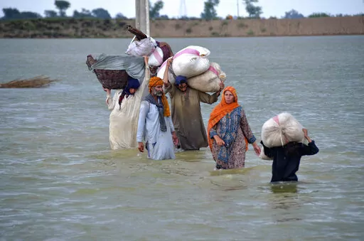 A displaced family wades through a flooded area after heavy rainfall, in Jaffarabad, a district of Pakistan's southwestern Baluchistan province, Aug. 24, 2022. A new study says human-caused climate change juiced the rainfall that triggered Pakistan's floods by up to 50%. But the authors of the Thursday, Sept. 15, study say other societal issues that make the country vulnerable and put people in harm's way are probably the biggest factor in the ongoing humanitarian disaster. (AP Photo/Zahid Hussa
