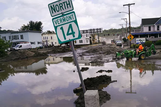 A small tractor clears water from a business as flood waters block a street, July 12, 2023, in Barre, Vt. Vermont has become the first state to enact a law requiring fossil fuel companies to pay a share of the damage caused by climate change, Thursday, May 30, 2024, after the state suffered catastrophic summer flooding and damage from other extreme weather. (AP Photo/Charles Krupa, file)