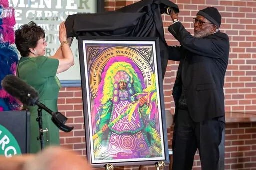 This photo provided by Faubourg Brewing Co. shows company owner Gayle Benson and Bertrand Butler, founder and executive director of the New Orleans Mardi Gras Indian Council, unveiling a poster being sold to benefit the council, Monday, Jan. 24, 2022, in New Orleans. The council also will get proceeds from 12-packs decorated with pictures of Mardi Gras Indians in their ornate regalia. (Maleah Pearson/Faubourg Brewing Co. via AP)