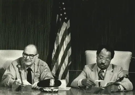 Retiring police Chief Henry Morris, left, and new Chief Warren Woodfork sit in the City Council chambers Wednesday, Jan. 16, 1985, prior to an awards ceremony for 1984's outstanding police officers. The New Orleans Police Department says its first Black superintendent has died. A tweet from the department says Warren Woodfork Sr. died Wednesday, March 9, 2022. The Times-Picayune/The New Orleans Advocate reports that he was 85 years old. (G. Andrew Boyd/The Times-Picayune/The New Orleans Advocate