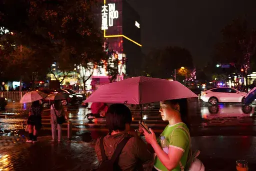 People look at their phones while waiting to cross an intersection in the rain at the Taikoo Li Sanlitun shopping center in Beijing, July, 30, 2024. (AP Photo/Vincent Thian, File)