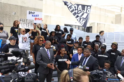 Legal team members Harry M. Daniels, bottom center right, speaks during a media press conference as legal team member Roderick Taylor, from left, in suit, Natassia Woods, mother of Le'Keian Woods, and legal team member Marwan Porter listen along with family, friends and or supporters gather Tuesday, Oct. 3, 2023 at the steps of the Jacksonville Sheriff's Office in Jacksonville, Fla. Attorneys for drug suspect Le'Keian Woods, who was repeatedly punched, elbowed and kneed by officers in northeast 
