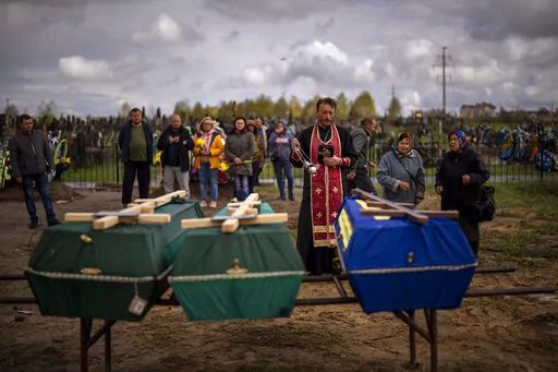 A priest blesses the remains of three people who died during the Russian occupation and were disinterred from temporary burial sites in Bucha, on the outskirts of Kyiv, on Wednesday, April 27, 2022. (AP Photo/Emilio Morenatti)